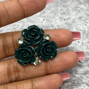 Op de afbeelding: Een cluster van drie donkergroene, roosvormige harsversieringen met heldere strasssteentjes. De versieringen zijn in een driehoekige vorm gerangschikt.