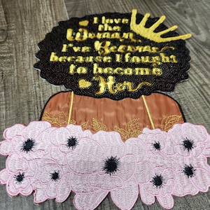 May include: Embroidered patch featuring a woman's silhouette with a black afro, a gold crown, and a pink floral collar. The text "I love the woman I've become because I fought to become her" is embroidered in gold.