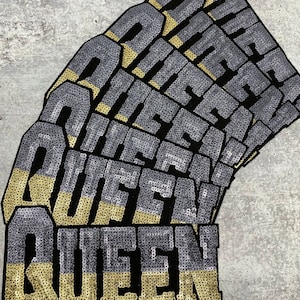 Pode incluir: Uma pilha de patches de lantejoulas pretas e douradas que soletram a palavra "QUEEN".