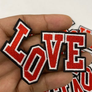 May include: Red felt "LOVE" letters with white outlines and black stitching. The letters are iron-on patches.