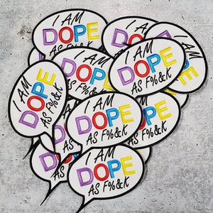 May include: A pile of colorful iron-on patches with the text "I am dope as f%&k" in a speech bubble design. The patches are in various colors, including purple, red, yellow, and blue.