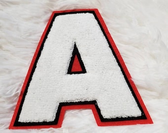 May include: White felt letter A with a red and black outline. The letter is on a white fluffy surface.