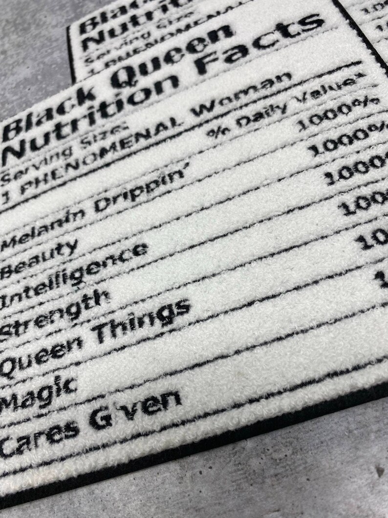 May include: White rectangular rug with black text that reads "Black Queen Nutrition Facts." The text includes phrases like "Melanin Drippin'," "Beauty," "Intelligence," and "Queen Things." The rug has a black border.