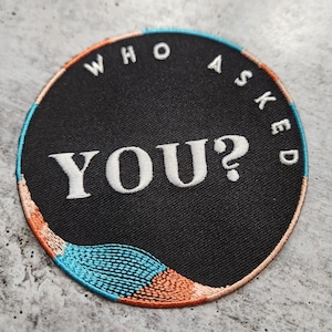 May include: A black and white embroidered patch with the text "WHO ASKED YOU?" in a white circle with a blue and orange wave design around the edge.