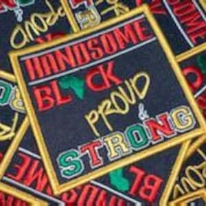 May include: A square iron-on patch with the words "Handsome Black and Proud & Strong" in gold embroidery. The words "Black" and "Strong" are in green and red embroidery. The outline of the patch is gold. The background is navy blue. An outline of the African continent is in the center of the patch.