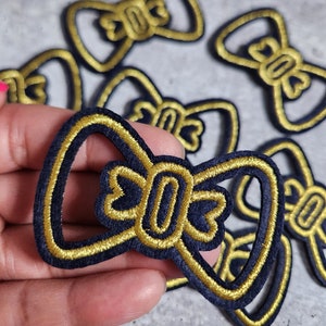 May include: A set of six gold and navy blue embroidered bowtie patches. The patches are about 2 inches wide and 1.5 inches tall.