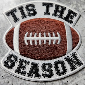 May include: White embroidered patch with a brown football in the center and the text "Tis the Season" in black.