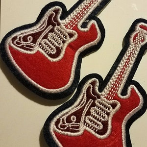 May include: Two red and white embroidered guitar patches with black outlines. The guitars have a white outline and a white string design.