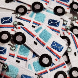 Pu&ograve; includere: Un mucchio di toppe ricamate bianche, blu e rosse con un camioncino postale dei cartoni animati con una busta blu. Il camioncino postale ha un tetto a strisce blu e bianche e i lati a strisce rosse e bianche.