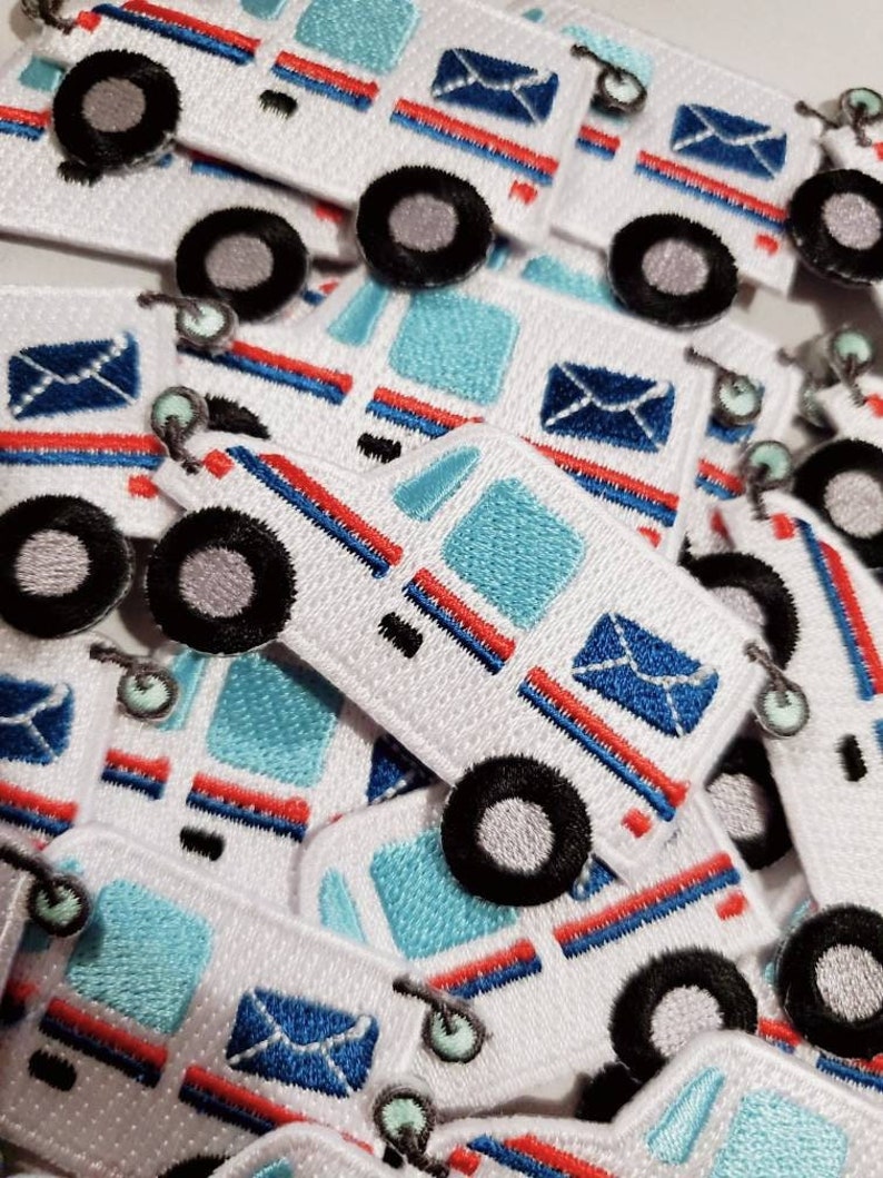 Pu&ograve; includere: Un mucchio di toppe ricamate bianche, blu e rosse con un camioncino postale dei cartoni animati con una busta blu. Il camioncino postale ha un tetto a strisce blu e bianche e i lati a strisce rosse e bianche.