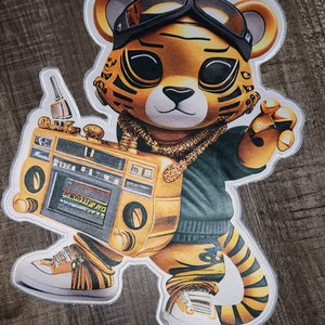 May include: A gold tiger wearing a green shirt, sunglasses, and a gold chain, holding a gold boombox. The tiger has a white background.