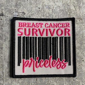 Puede incluir: Un parche blanco con ribete negro presenta un código de barras rosa con el texto "Breast Cancer Survivor" y "priceless" debajo del código de barras.