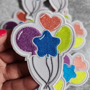 Könnte beinhalten: Ein Set mit fünf bunten, gestickten Bügelbildern mit einem Bündel Ballons mit Sternen und Herzen. Die Ballons sind lila, grün, blau, rosa und orange.