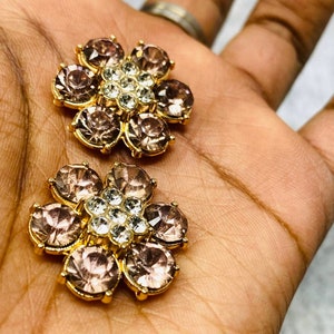 May include: Two gold-toned flower-shaped brooches with clear and pink rhinestones.