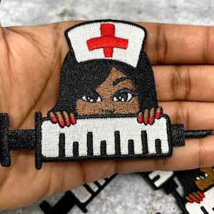 May include: Iron-on patch featuring an embroidered cartoon nurse with a syringe. The nurse is wearing a white hat with a red cross and has brown skin and long black hair. The syringe is black and white with a red needle.