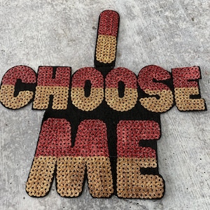 May include: A gold and red sequined patch with the words "I CHOOSE ME" on it.