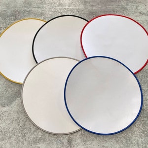 Könnte beinhalten: Fünf leere, runde Patches mit verschiedenen farbigen Nähten an den Rändern. Die Patches sind weiß mit einer glatten Oberfläche und sind in einem Kreis auf einem grauen Hintergrund angeordnet.