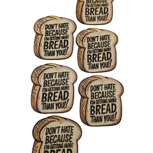 May include: A collection of six embroidered patches shaped like slices of bread. Each patch features a tan crust and a cream-coloured centre with the black embroidered text: DON'T HATE BECAUSE I'M GETTING MORE BREAD THAN YOU!! in a bold, sans-serif font.