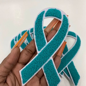 May include: A set of teal blue ribbon patches with white outlines. The patches are made of a soft, fuzzy material and are perfect for adding a touch of color and support to clothing, bags, or other items.