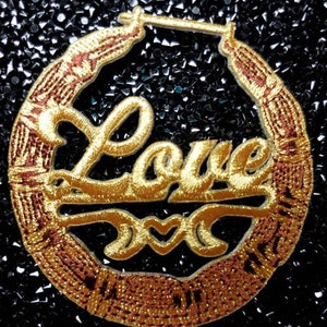 May include: Gold hoop earrings with a red and gold design. The earrings feature the word "Love" with a heart symbol.