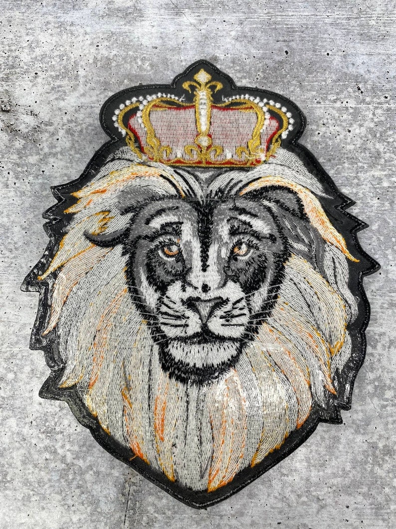 K&ouml;nnte beinhalten: Gestickter L&ouml;wenkopf-Patch mit einer goldenen Krone. Der L&ouml;we hat eine wei&szlig;e M&auml;hne und ein schwarzes Gesicht. Die Krone hat rote und goldene Akzente.