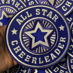 May include: Purple and white embroidered patch with the text "All Star Cheerleader" and a star in the center.