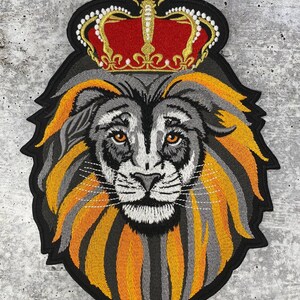 Puede incluir: Parche bordado de la cabeza de un león con una corona dorada con joyas rojas. El león tiene una melena gris y naranja.