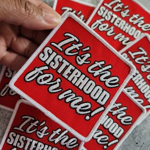 May include: Red and white embroidered patches with the text "It's the SISTERHOOD for me!". The patches have a white border and are square with rounded corners. Several patches are visible.