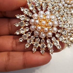 May include: A gold-toned brooch with a cluster of white pearls in the center and a surrounding ring of clear rhinestones.