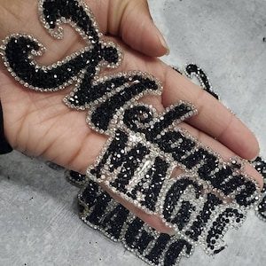 May include: A close-up of a black and white rhinestone iron-on patch that says "Show Me Magic".