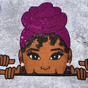 May include: A brown-skinned woman with large eyes peeks over a surface. She is wearing a purple sequined head wrap and small pink earrings. Her hands are outstretched, pointing to the sides.