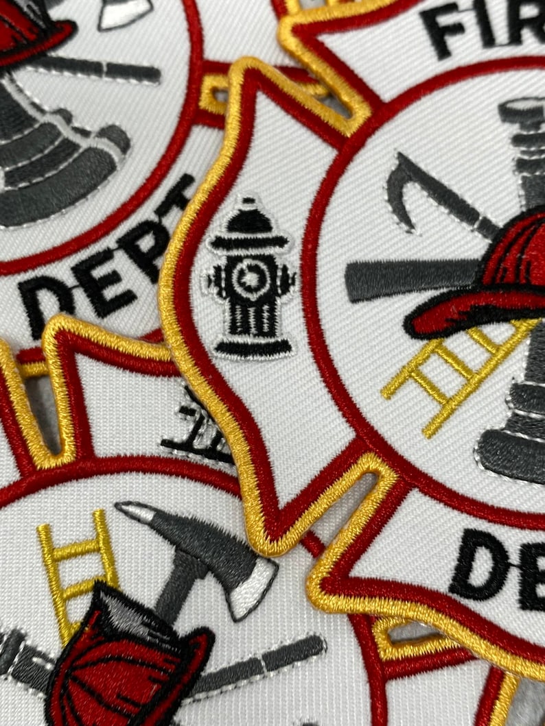 Op de afbeelding: Close-up van een set geborduurde patches met een brandweerthema. De patches zijn wit met rode en gouden randen. Ze bevatten een brandkraan, een ladder, een bijl en een brandweerhelm.