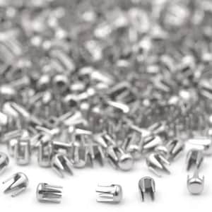 May include: A collection of small, shiny, silver-colored metal rivets. The rivets have a rounded top and a three-pronged base. The image shows a close-up view of the rivets, with some in focus and others blurred in the background.