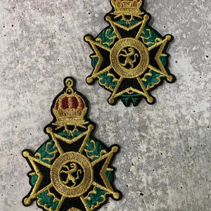 May include: Two gold embroidered patches with a black cross, green leaves, and a gold lion in a circle. The top of each patch features a gold crown with red and white accents.