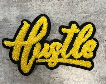 Könnte beinhalten: Gelber gestickter Aufnäher mit dem Wort "Hustle" in einer stilisierten Schrift.