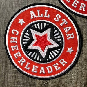 May include: Red and white embroidered patch with a star in the centre and the text "ALL STAR CHEERLEADER" around the star.