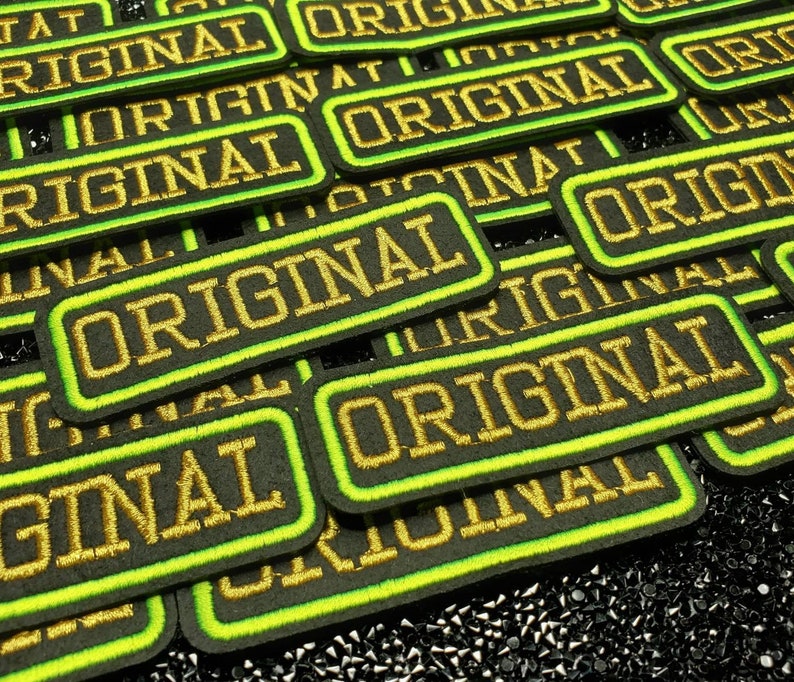 May include: Close-up of multiple black and green embroidered patches with the word "ORIGINAL" in gold thread.