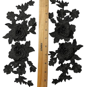 May include: Two black floral lace appliques with a wooden ruler for scale. Each applique features detailed rose and leaf designs. The ruler is marked in inches, showing the appliques are approximately 25 cm in length.