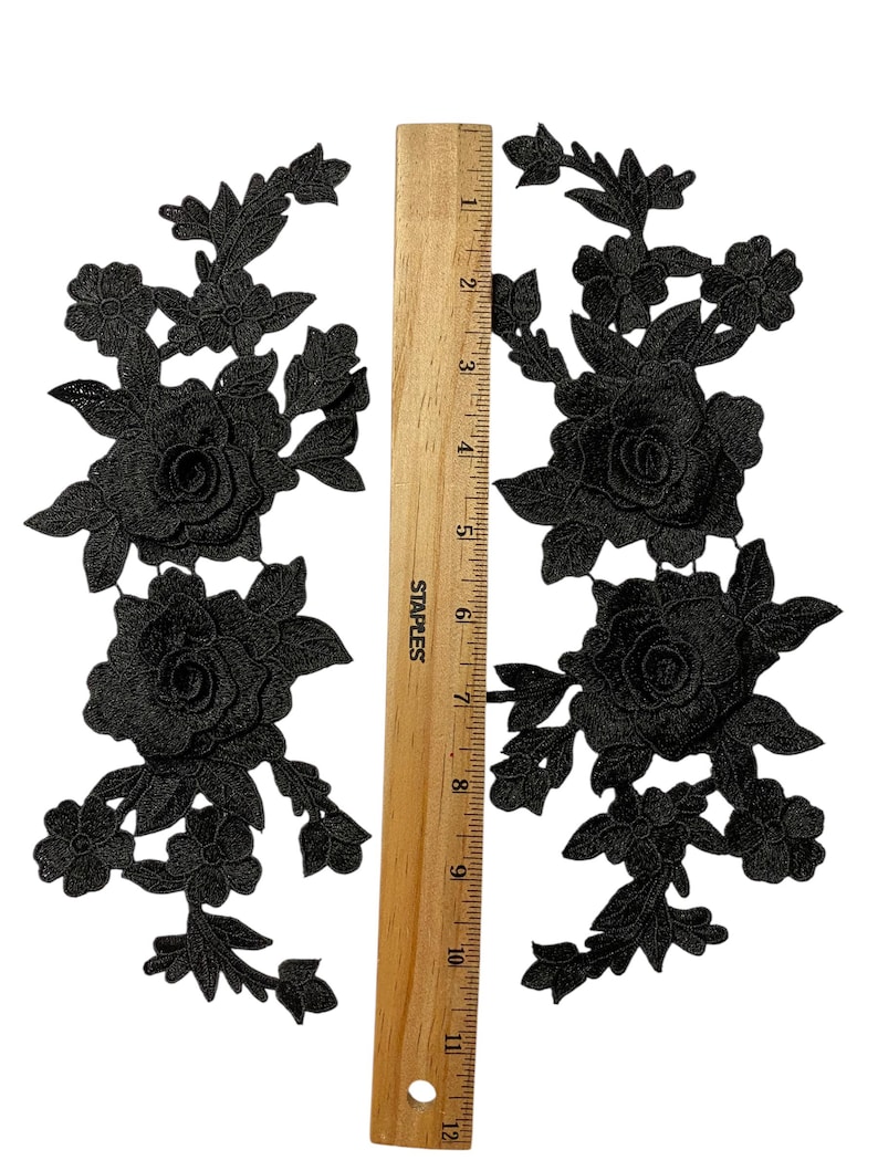 May include: Two black floral lace appliques with a wooden ruler for scale. Each applique features detailed rose and leaf designs. The ruler is marked in inches, showing the appliques are approximately 25 cm in length.