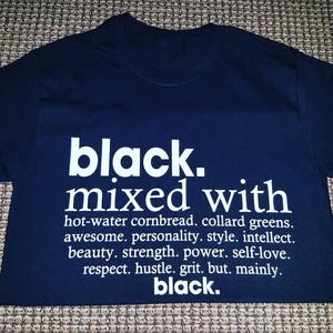 May include: Black t-shirt with white text that reads "black. mixed with hot-water cornbread. collard greens. awesome. personality. style. intellect. beauty. strength. power. self-love. respect. hustle. grit. but. mainly. black."