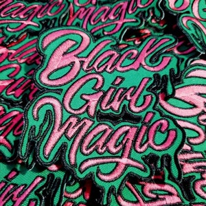 Pode incluir: Um close-up de vários patches bordados verdes e rosa que dizem "Black Girl Magic".