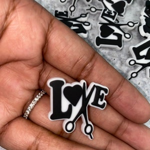 May include: White and black plastic charms with the word "LOVE" and a pair of scissors with a heart in the middle.