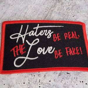 May include: Black embroidered patch with red stitching. The patch reads "Hatters be real. The love be fake!"