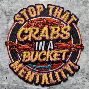 May include: A black and yellow embroidered patch with the text "Stop That Crabs In A Bucket Mentality!"  The patch features a red, orange, and yellow crab design.