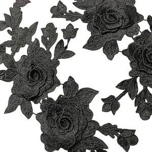 May include: Close-up of black floral lace appliques. The appliques feature detailed embroidered roses, buds, and leaves. The lace is intricately designed with a textured appearance, ideal for embellishing garments or crafts.