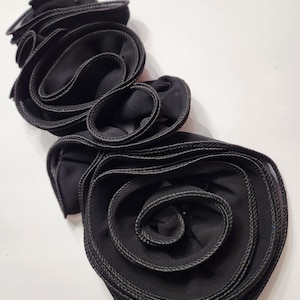 May include: A black fabric flower with layered, ruffled petals and a stitched edge. The flower is a decorative accessory, possibly for clothing or crafts. The design features a spiral center and multiple layers of fabric.