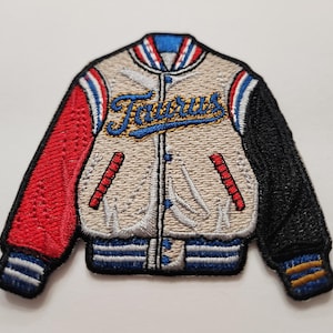 May include: A beige, red, and black embroidered iron-on patch of a varsity jacket with the word "Taurus" in blue and gold lettering.