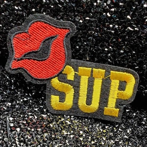 May include: Two embroidered patches, one red and shaped like a lip, the other yellow with the word "SUP" on a black background.