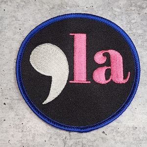 May include: A black and blue circular patch with a white semicolon and the word "la" in pink.