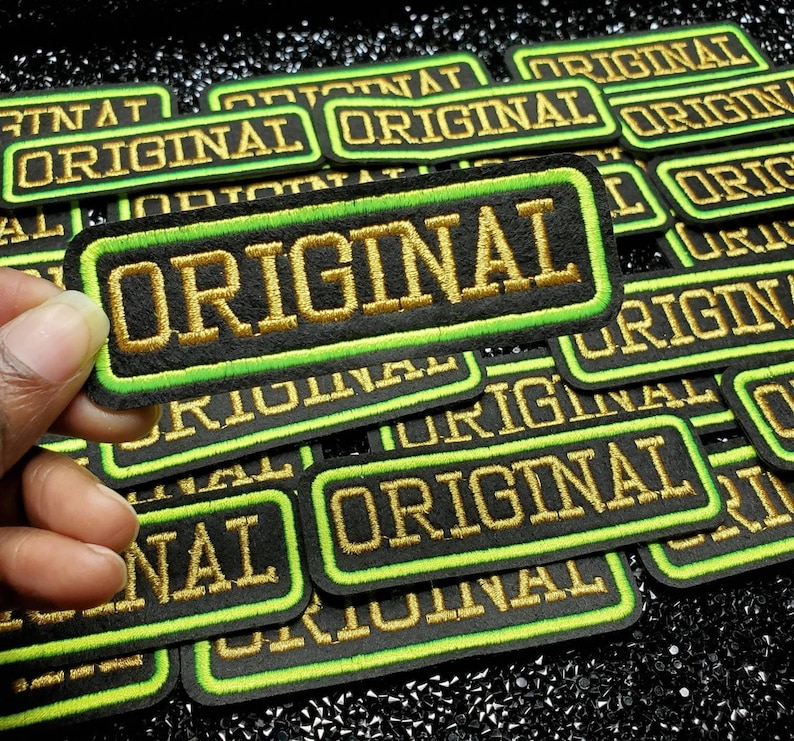 May include: A pile of black and green iron-on patches with gold embroidery that reads "ORIGINAL".